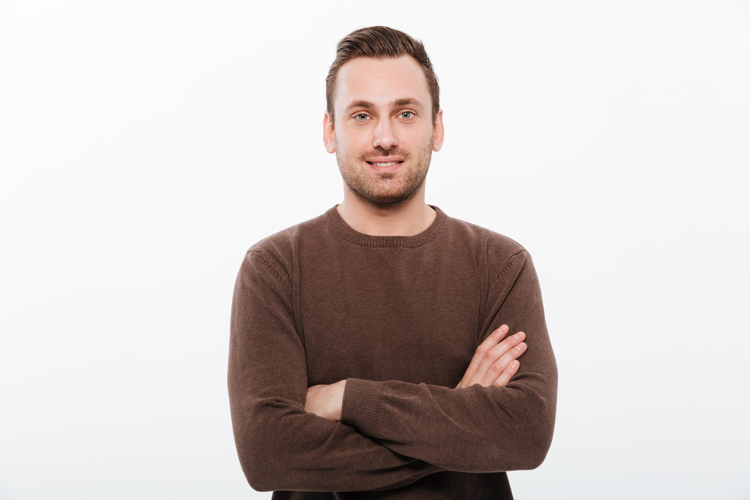 Image of handsome young cheerful man standing isolated over white background with arms crossed. Looking camera.