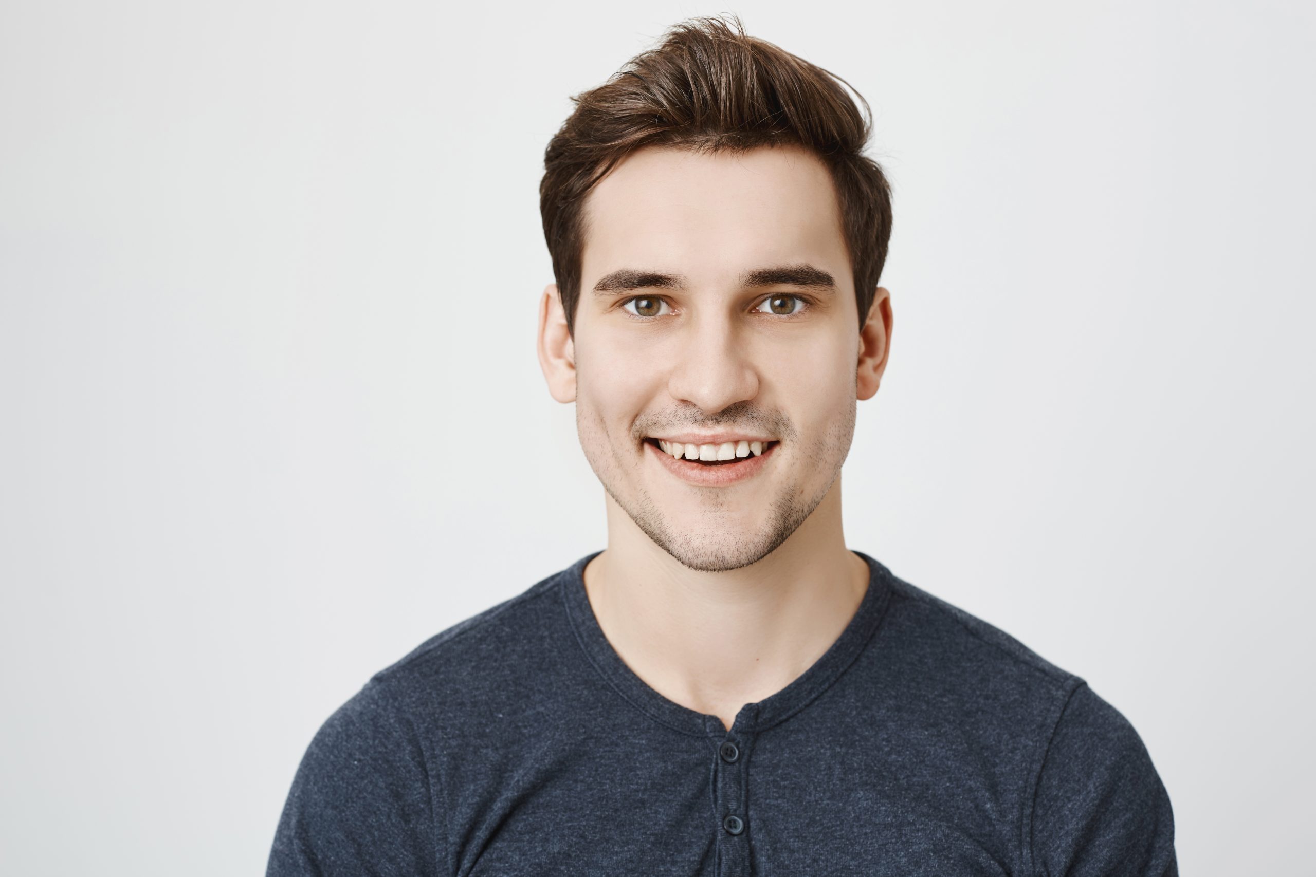 Portrait of good-looking stylish bearded male with happy expression of face, smiles broadly, isolated against gray background. Male expresses positive emotions and feelings